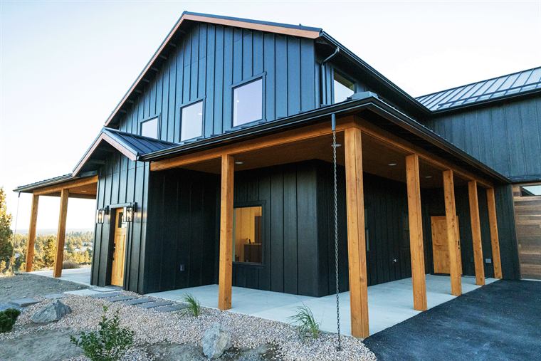 Barndo exterior with black siding and a cedar-post porch under a blue sky