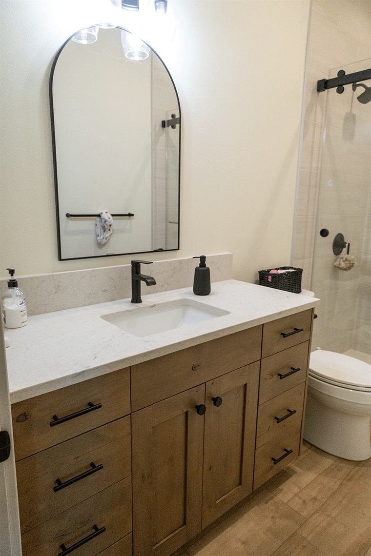 Bathroom vanity with wood cabinets and an arched black mirror