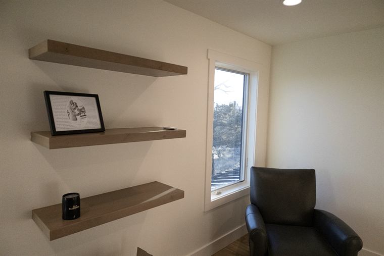 Floating wood shelves and a black leather chair by a window