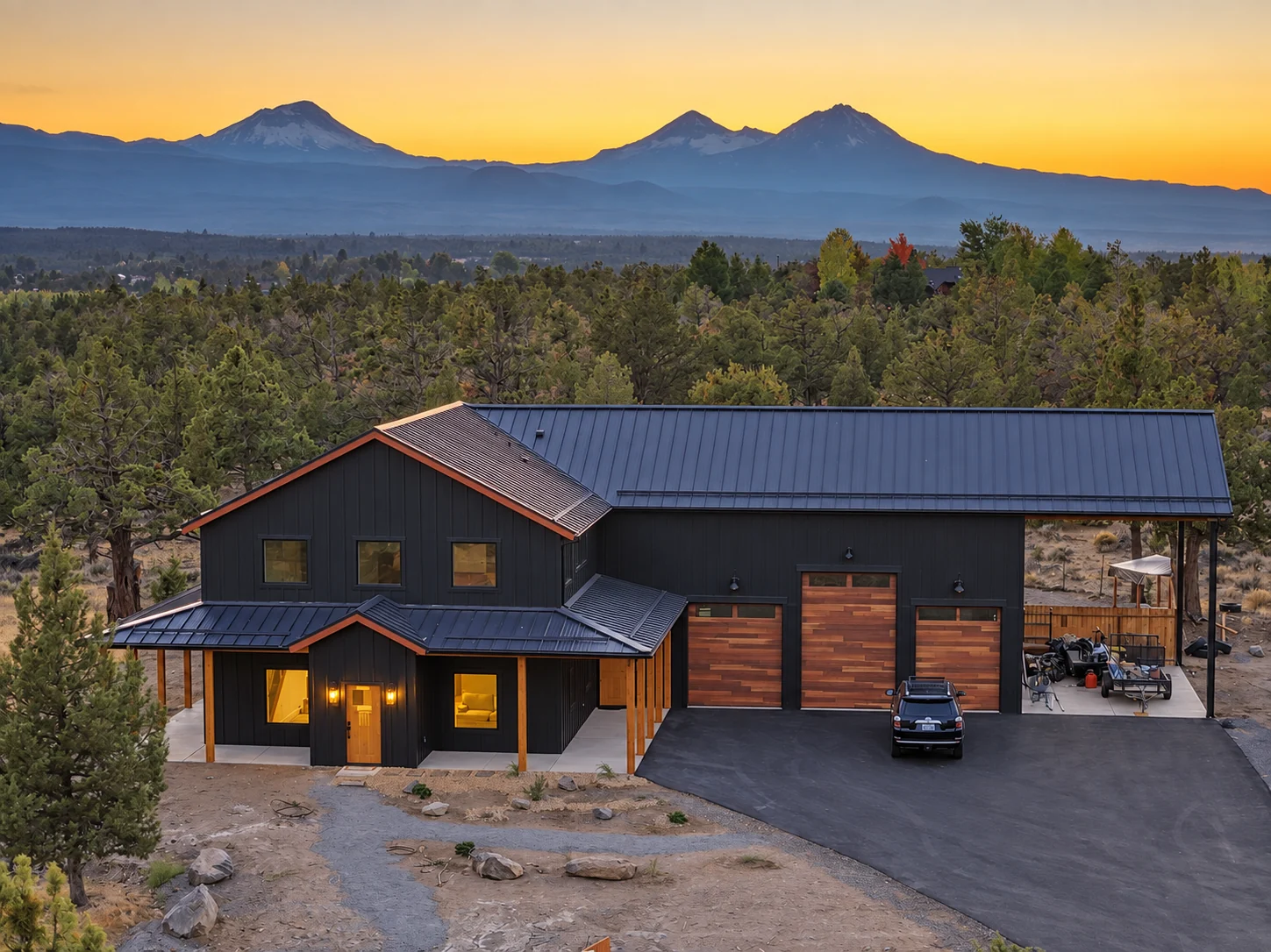 Aerial view of a dark-sided barndominium High Desert Homes built, with the Cascade mountains at sunset behind it