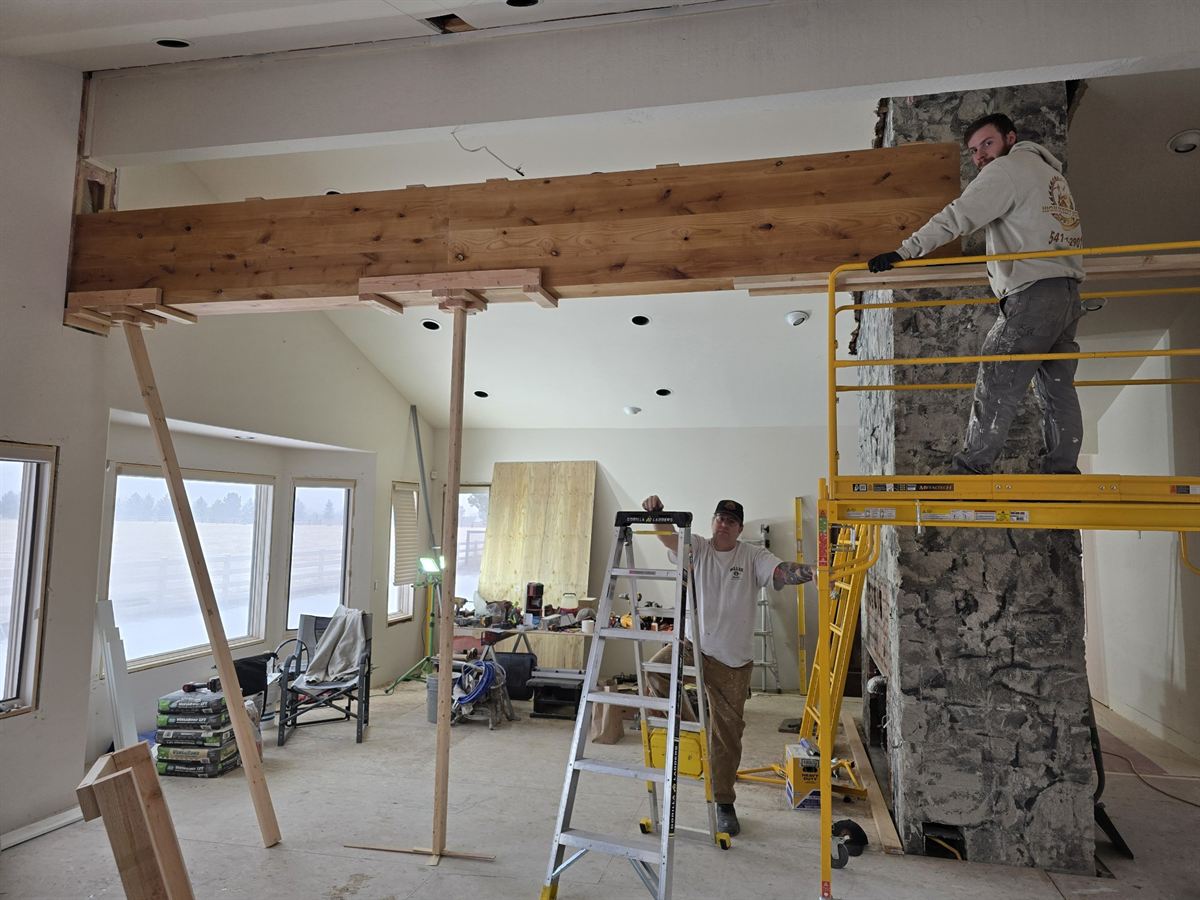 Interior under construction with scaffolding, exposed beams and a stone fireplace in progress