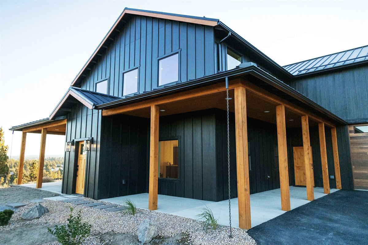 Board-and-batten barndominium with a timber-framed porch under a blue sky