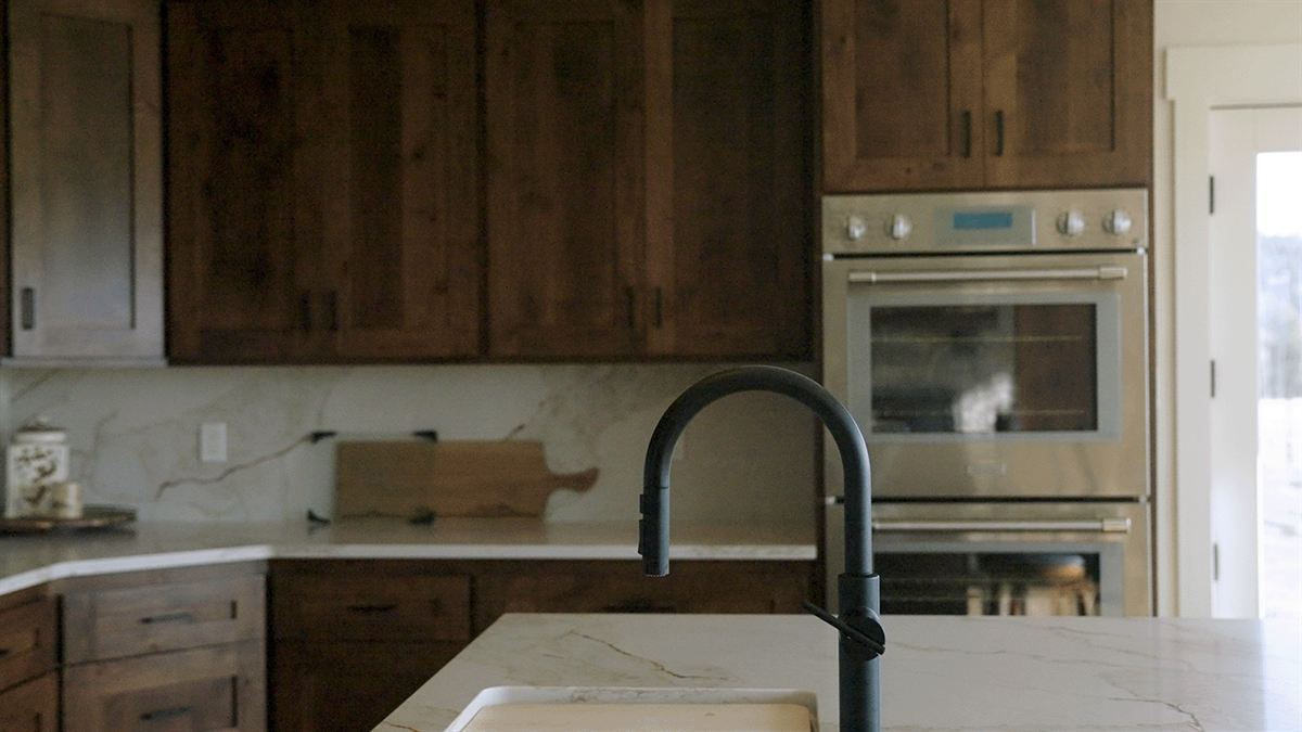 Remodeled kitchen with dark wood cabinets, a wall oven and a black faucet